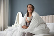© New Africa - Beautiful young woman wrapped with soft blanket holding cup of hot drink on bed at home