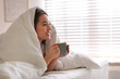 © New Africa - Beautiful young woman covered with warm blanket enjoying hot drink on bed at home. Space for text