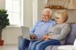 © Studio Romantic - Laughing senior happy couple sitting on sofa at home and watching funny movie or online show on laptop together. Elderly people happy lifestyle and modern technologies concept
