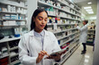 © StratfordProductions - Young female woman wearing labcoat working in chemist using digital tablet
