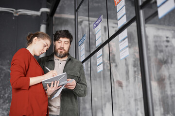 Waist up portrait of two business people standing by glass wall while planning project in modern office, copy space