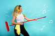© alphaspirit - Funny housewife use broom like a rock guitar. cyan background