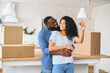 Relocation concept. A smiling cheerful multiracial couple in embraces holding keys stating in new apartment among cardboard boxes, bought real estate, newlyweds get a mortgage
