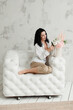 © Natalia - brunette girl with bare feet and a bouquet of flowers sits on a white armchair