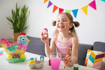 Wall Mural - happy girl paints Easter eggs at home against background of bright decor. kids craft. create art for children