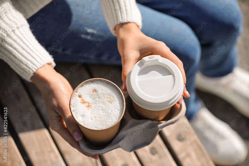 Woman with takeaway cups of tasty latte outdoors, closeup - obrazy, fototapety, plakaty 