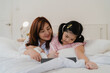 © tirachard - Asian grandmother using tablet read fairy tales to granddaughter at home. Senior Chinese, grandma happy relax with young girl before bedtime lying on bed in bedroom at home at night concept.