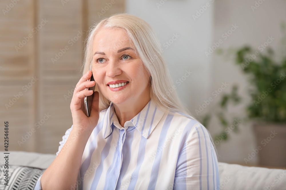 Happy mature woman talking by phone at home