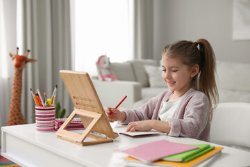 Canvas Print - Adorable little girl doing homework with tablet at table indoors