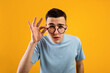 Young Caucasian man in glasses being skeptical, looking suspicious, having some doubt on orange studio background