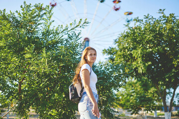 Half length portrait of teenage Caucasian woman with backpack resting on summer leisure enjoying sunny weather in park, young hipster girl 20s in casual wear walking during free time on weekend