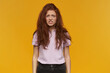 © timtimphoto - Portrait of frowning, irritated lady with long ginger messy hair. Wearing pink t-shirt. People and emotion concept. Just woke up. Watching at the camera, isolated over orange background