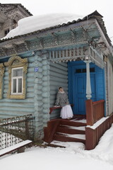 Wall Mural - Woman in Orenburg shawl, scarf. Wooden rural house with carved windows in russian village, Nizhny Novgorod region, Russia. Russian folk style in countryside architecture, fashion. Countryside, country