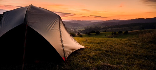 Tourist tent in the mountains under dramatic evening sky. Colorfull sunset in mountains. Camping travell concept. Traveler people enjoying the advanture alternative vacation