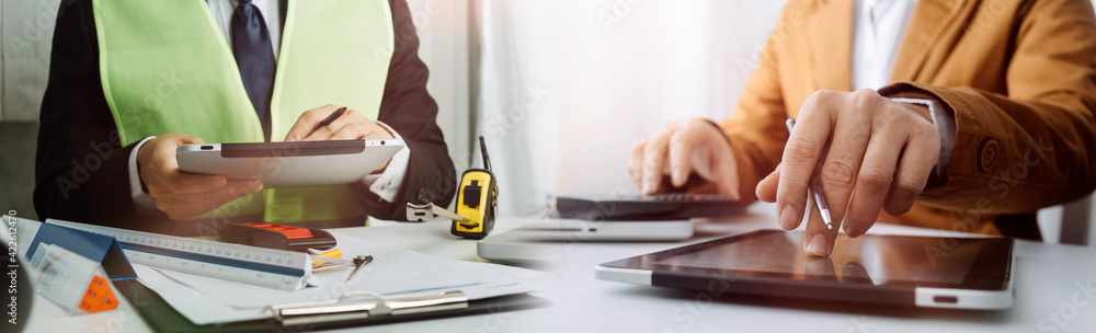 Two colleagues discussing data working and tablet, laptop with on on architectural project at construction site at desk in office - obrazy, fototapety, plakaty 