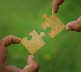 Teamwork and partnership concept. Hands holding up one, alone wooden jigsaw puzzle against green and yellow bokeh