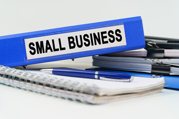 On the table are a notebook, a pen, documents and a folder with the inscription - SMALL BUSINESS