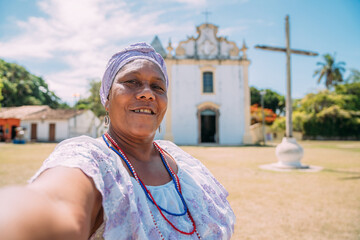 Wall Mural - Happy Brazilian woman of African descent dressed in the traditional Bahian dress making a selfie in front of the church. focus on face