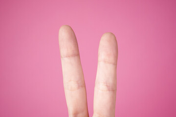 Closeup of a person doing the peace sign against a pink background