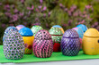 Hand-made Easter eggs on a green pedastal in front of purple lavender flowers.