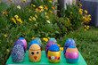 Hand-made Easter eggs on a green pedastal in front of yellow and orange spring flowers