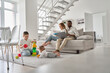 © insta_photos - Multiethnic family spending time together in new home. Mixed race diverse children playing toys on carpet while multiracial parents using laptop and reading book sitting on couch in house living room.
