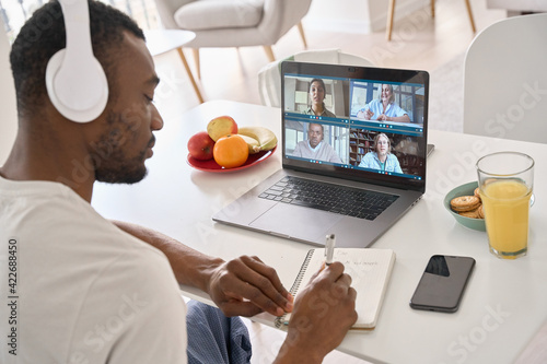 African Black business man having virtual team meeting on video conference call using laptop distance working from home office with diverse people group in team online remote chat. Over shoulder view