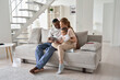 © insta_photos - Happy young multi ethnic diverse parents having fun using digital tablet computer holding cute little mixed race baby child daughter sitting on couch in modern cozy living room at home together.