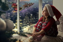 Cute Little Girl On Window Sill At Home Waiting For Santa Claus. Christmas Celebration