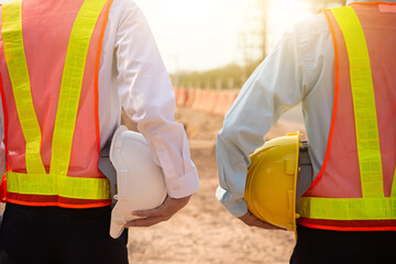 Two worker holding yellow helmet and white helmet on site construction background