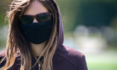 Portrait of a girl with dreadlocks in a protective medical mask. Girl in glasses and a hood.