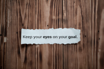 Inspirational quote - Keep your eyes on your goal. Notes message on white rip paper note on brown wooden wall background. Business goals motivational words concept.