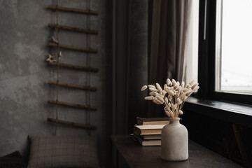 Rabbit bunny tail grass bouquet in pot, books stack on table against window