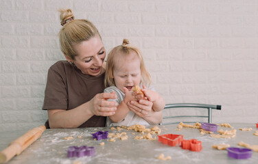 happy young mother and her little daughter together prepare delicious cookies sitting at the table in the home kitchen