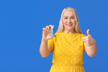 Wall Mural - Mature woman with inhaler showing thumb-up on color background