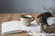 Eine rustikale Kaffeetasse auf einem offenen Buch und Strickzeug in einem Korb auf einem braunen Holztisch. Vitage Stil, Hygge.