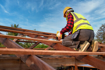 Asian roofer working on roof structure of building on construction site, Roofer using air or pneumatic nail gun and installing on wooden roof structure.