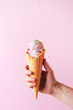 Fototapeta Tulipany - Female hand holding the pink ice cream with falling sprinkles in waffle cone