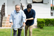 © NVB Stocker - Elderly Asian father and Adult son walking in backyard. Positive Asian man caregiver helping patient