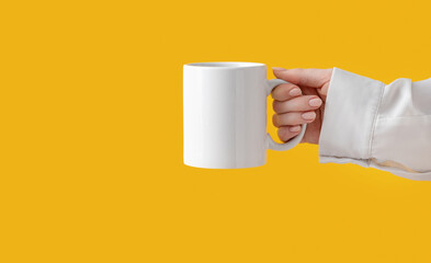 mockup ceramic white coffe cup or mug in female hands on yellow background with copy space. Blank template for your design, branding, business. Real photo. Woman in shirt casual style