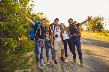 Wall Mural - group of young smiling tourists hikers standing on road together and feeling excited