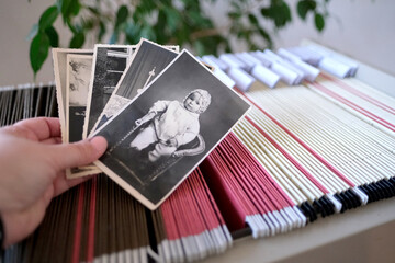 hands hold a stack of vintage photographs lies on an archival metal cabinet with thin files with information in room, home archive with folders, selective focus, filing cabinet