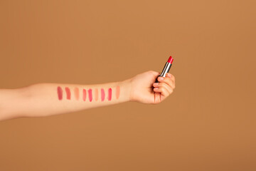 Wall Mural - Cropped view of woman testing different colors of lipstick on her hand, brown studio background