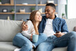 Happy loving interracial couple relaxing at home, watching tv and drinking coffee