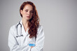 © Monkey Business - Studio Portrait Of Stressed Young Female Doctor Wearing White Coat Against Plain Background