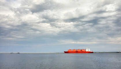 Red LNG tanker in port with stormy cloudscape.