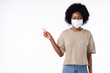 African teen girl pointing at copy space in medical mask against Covid 19 isolated in white