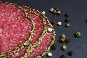 Makro closeup of slices french fresh salami with mixed pepper crust with peppercorns on black slate stone board