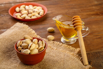 Pistachios on burlap next to honey with a spoon on a wooden table.