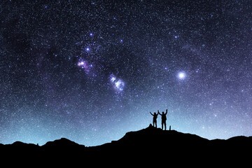 Wall Mural - two hikers silhouettes stands on the hill and looking at the bright starry sky orion galaxy. beautif